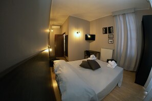 Une chambre d’hôtel avec un grand lit, un bureau, un téléviseur à écran plat et une fenêtre avec des rideaux.