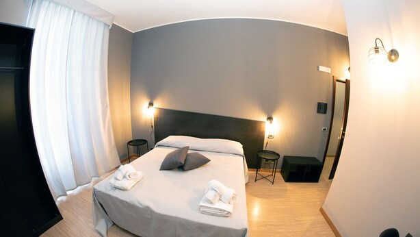 Una habitación de hotel moderna con techo curvo, una cama grande con cabecera, dos mesitas de noche, un espejo y un armario.