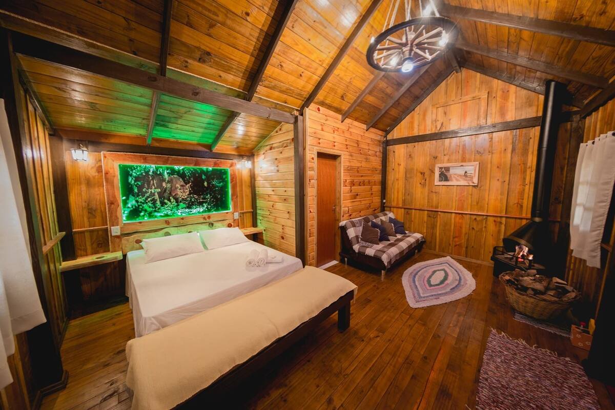 Een knus houten kamer met een bed, een stoel, een open haard en een tv aan de muur.