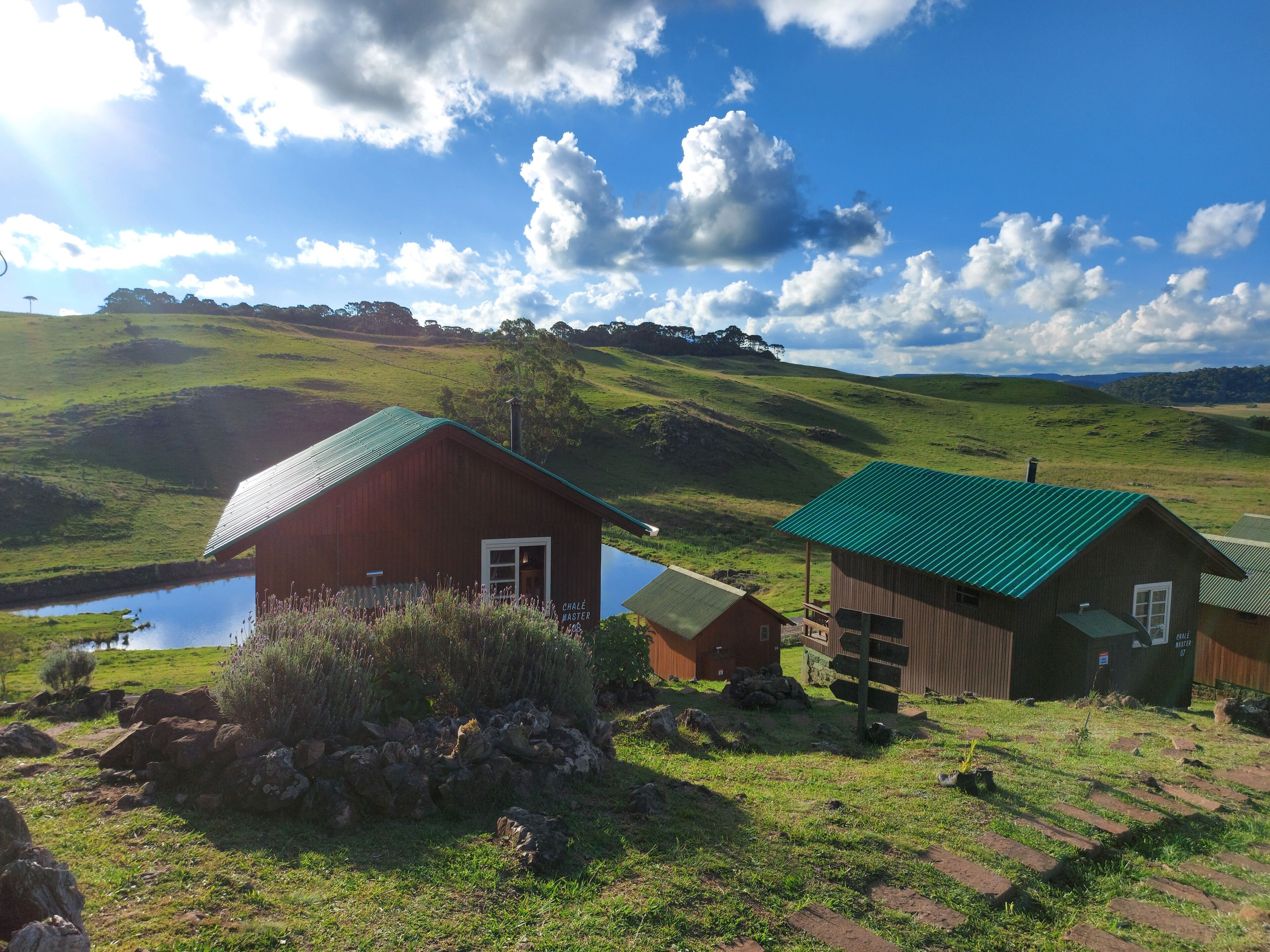 Uma cabana rústica com telhado verde e um pequeno lago próximo.