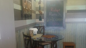 A cozy room with a wooden wall, a glass table, and a red cushioned chair. A chalkboard with "Rude Ranch Welcome you" is visible. - Glamping Tent! Nestled at base of Mission Mountains! Quiet & secluded.  (Ronan)
