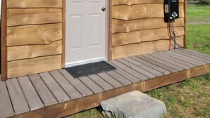 A wooden cabin with a white door, a welcome sign, a sign requesting shoe removal, and a power outlet with a Gaglio brand charger. - Glamping Tent! Nestled at base of Mission Mountains! Quiet & secluded.  (Ronan)