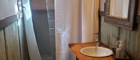 Un baño con tocador de madera, lavamanos blanco, cortina de ducha y espejo.