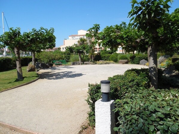 A paved pathway in a landscaped area with trees and shrubs, leading to a building with multiple balconies.