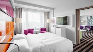Une chambre d’hôtel avec un grand lit, un bureau avec une chaise, une télévision et une vue sur la ville par la fenêtre.