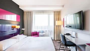A hotel room with a large bed, a desk with a chair, a television, and a window with curtains.