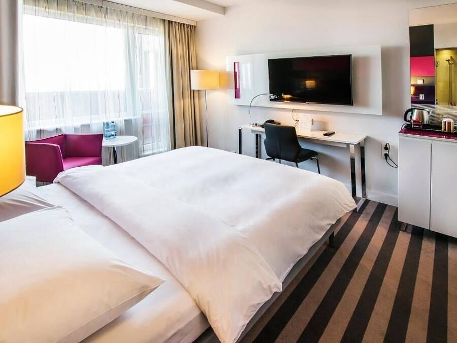 A hotel room with a large bed, a desk, a TV, a chair, and a small table.