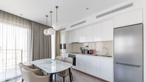 A modern kitchen with white cabinets, a stainless steel refrigerator, and a dining area with a marble table and leather chairs. - Comfortable 2BR Address Harbour Point (Dubai)