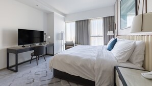 A hotel room with a bed, a desk with a TV, a chair, and a window with curtains. - Comfortable 2BR Address Harbour Point (Dubai)