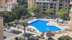 Un quartier résidentiel doté d’une piscine, entourée de verdure et bordé de voitures garées.