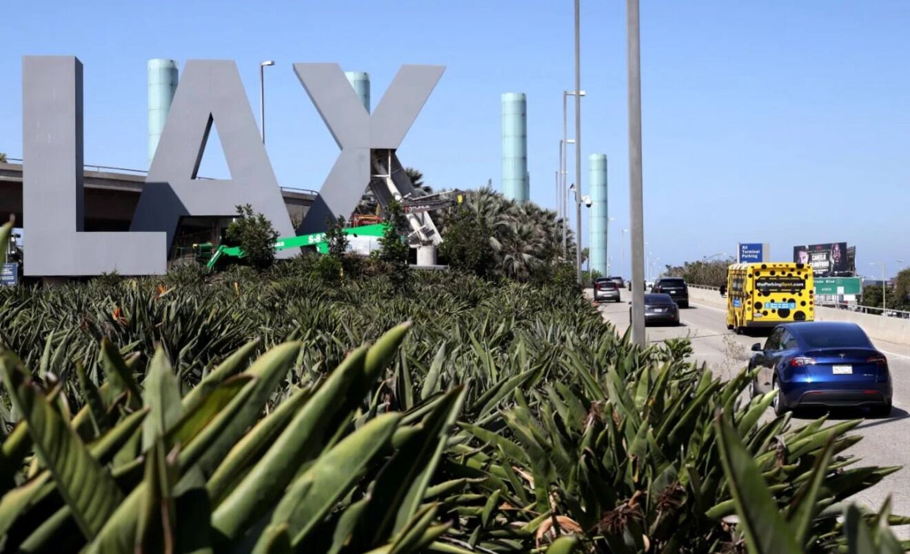 Un gran cartel con la indicación 'LAX', con una excavadora cerca, rodeado de vegetación.