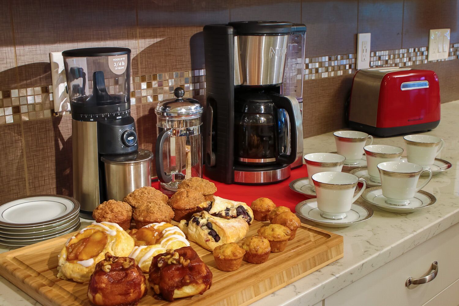 A kitchen counter with various coffee makers, a toaster, and a tray of pastries.
