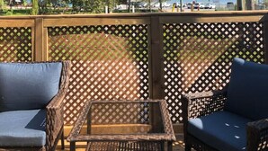 Une terrasse dotée de meubles en osier et offrant une vue sur les arbres et un plan d’eau.