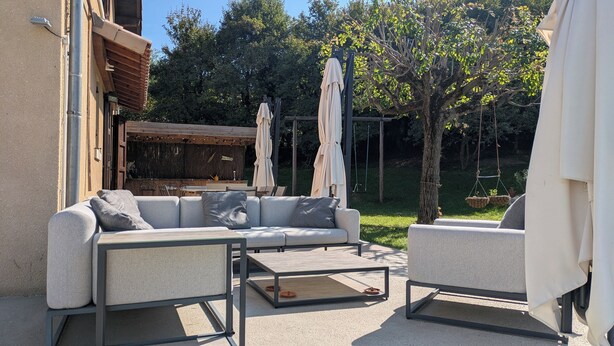 Un patio al aire libre con un sofá, sillas y una mesa. Hay sombrillas y una pérgola de madera.