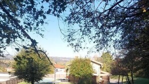 Un jardín con un bancal elevado, un árbol pequeño y un edificio al fondo.