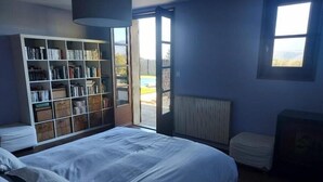 Un dormitorio con una cama grande, una estantería, un radiador y una ventana con vistas.