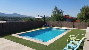 Una piscina rectangular con agua cristalina azul, rodeada de césped artificial verde y un patio de piedra.