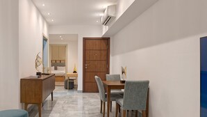 A modern hotel room with a wooden dining table, four chairs, a blue ottoman, a wooden cabinet, and a large wooden door. - VESTA - New Cairo Residence (New Cairo)