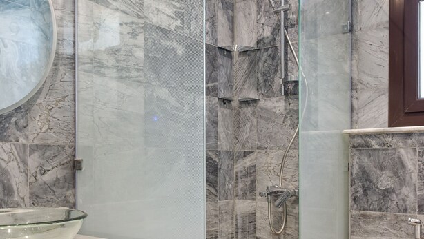 Une salle de bain moderne avec une douche à parois de verre, des murs en marbre et un lavabo en forme de bol en verre.