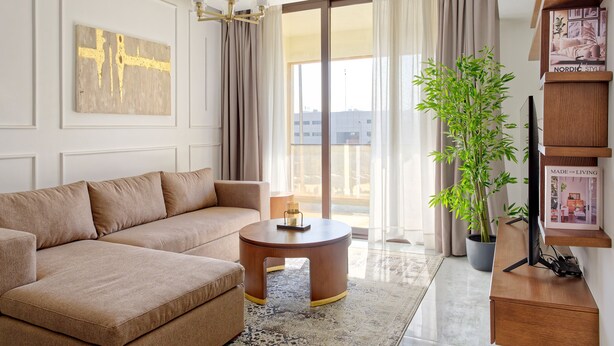A modern living room with a beige sectional sofa, a round coffee table, a potted plant, and a bookshelf. - VESTA - New Cairo Residence (New Cairo)
