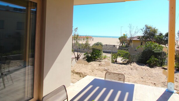 A balcony with a view of the beach, a table, and a chair. - Athesis Lodges (Rosolina Mare)
