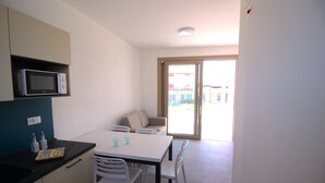 A small, modern kitchen with a microwave, a dining table with chairs, and a sofa in the adjacent living area. - Athesis Lodges (Rosolina Mare)