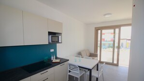 A modern kitchen with white cabinets, a black countertop, and a microwave. There is a dining table with white chairs and a glass of water on it. - Athesis Lodges (Rosolina Mare)