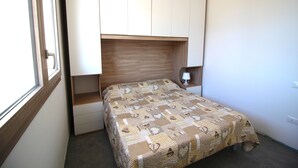 A bedroom with a bed, a wooden headboard, a bedside table with a lamp, and a window. - Athesis Lodges (Rosolina Mare)