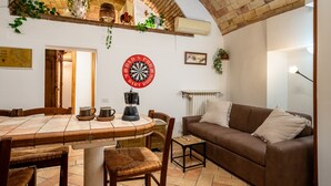 Een gezellige woonkamer met een dartbord, een bruine leren bank, een bijzettafeltje en een eettafel met stoelen.