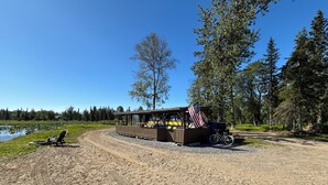 Eine rustikale Holzhütte mit einem Feldweg, der zu ihr führt, umgeben von Bäumen und einem See.