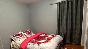 A neatly made bed with a floral bedspread, a dark curtain, and a wooden floor. - Glamour Room C 6mins to Newark Liberty (Newark)
