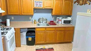 A compact kitchen with wooden cabinets, a gas stove, a microwave, and a trash bin. A 'No Smoking' sign is visible on the wall. - Glamour Room C 6mins to Newark Liberty (Newark)