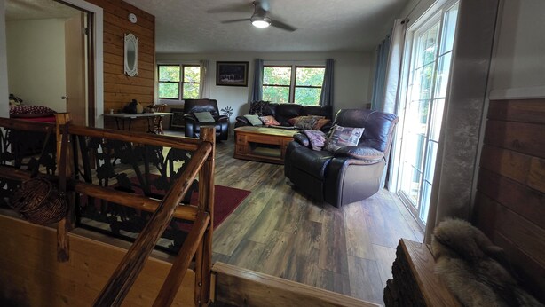 A spacious living room with a wooden floor, a leather sofa, a dining table with chairs, and a large window providing natural light. - Private 3-bedroom farmhouse in Rural Roseau (Roseau)