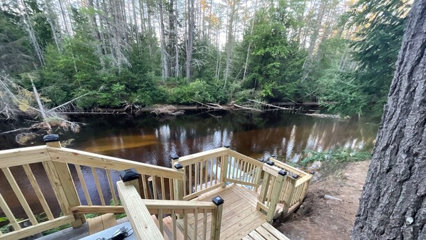 Eine Holzterrasse mit Geländern, die auf einen Fluss mit umgebenden Bäumen blickt.