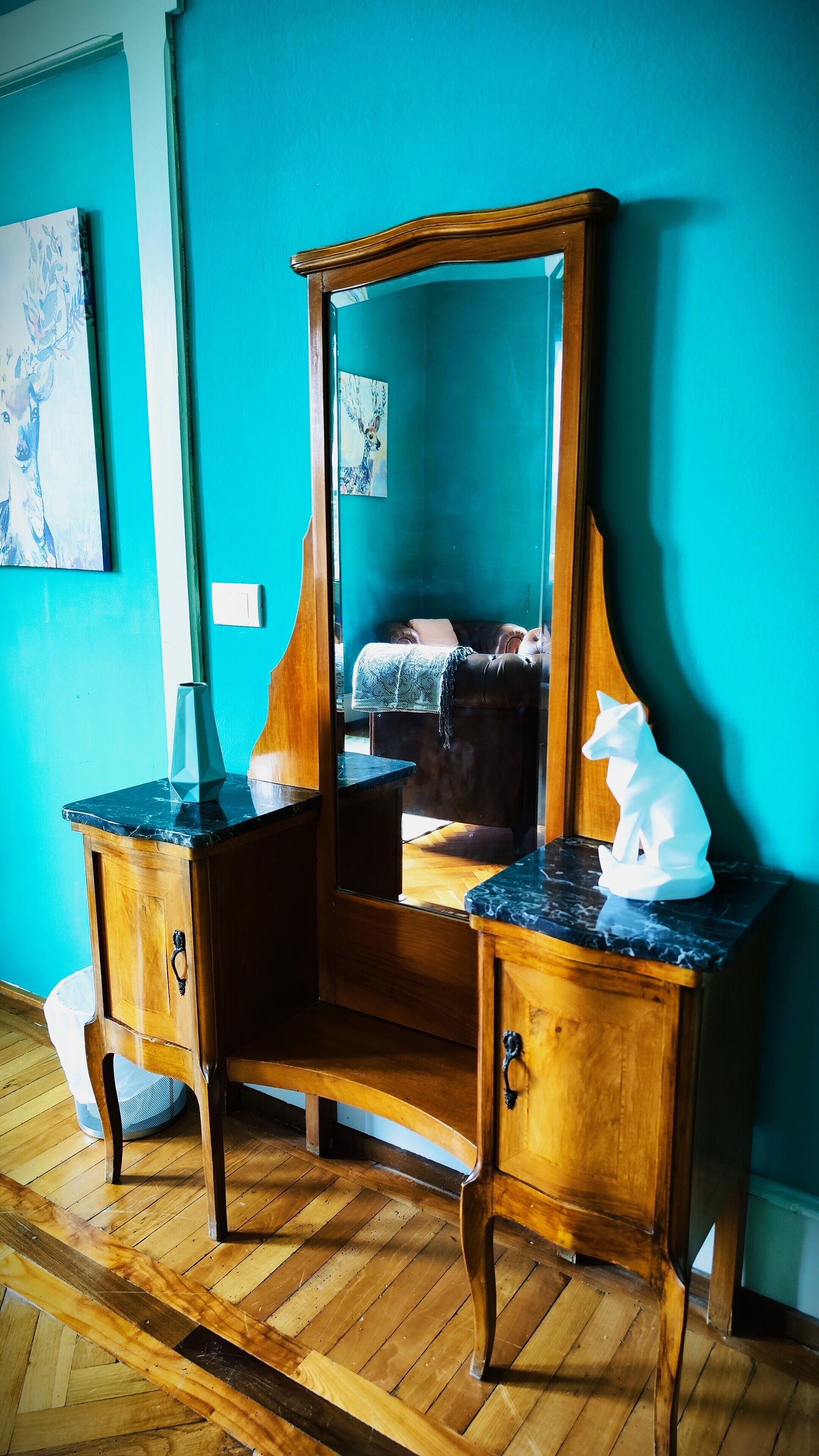 Une commode en bois avec un miroir, un vase et une sculpture de chat blanc.