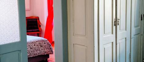 A hallway with a patterned floor, a bed with a patterned bedspread, and a red curtain in a room.