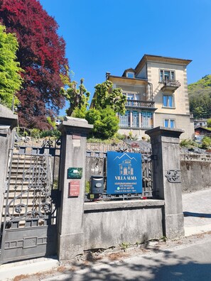 A villa with a gated entrance, a blue signboard, and a building with balconies. - Villa Alma Lake Como (Centro Valle Intelvi)
