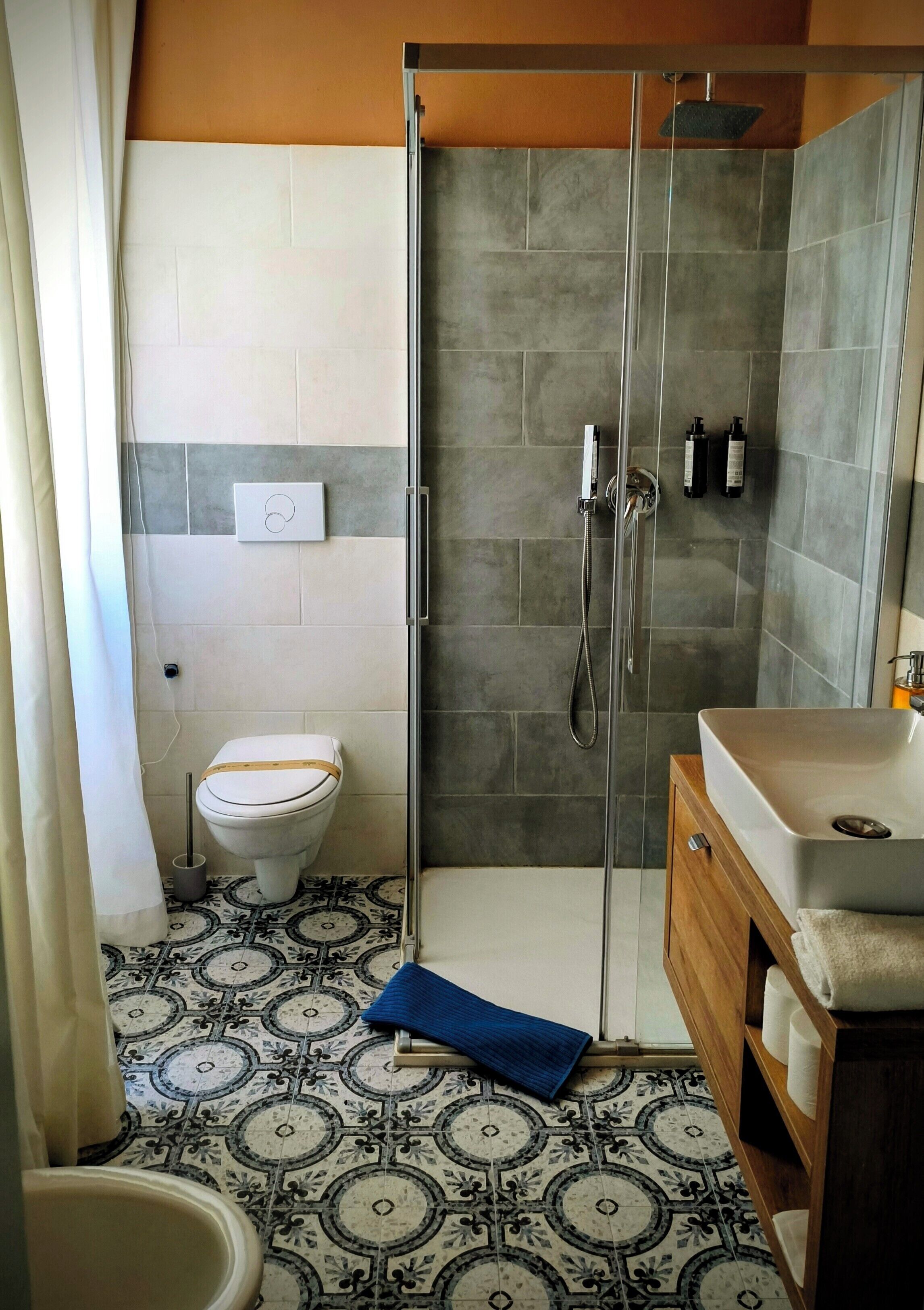 A bathroom with a shower, toilet, sink, and patterned floor tiles.