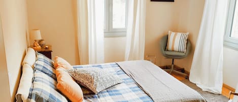 A bedroom with a bed, a chair, a lamp, and a window with curtains.