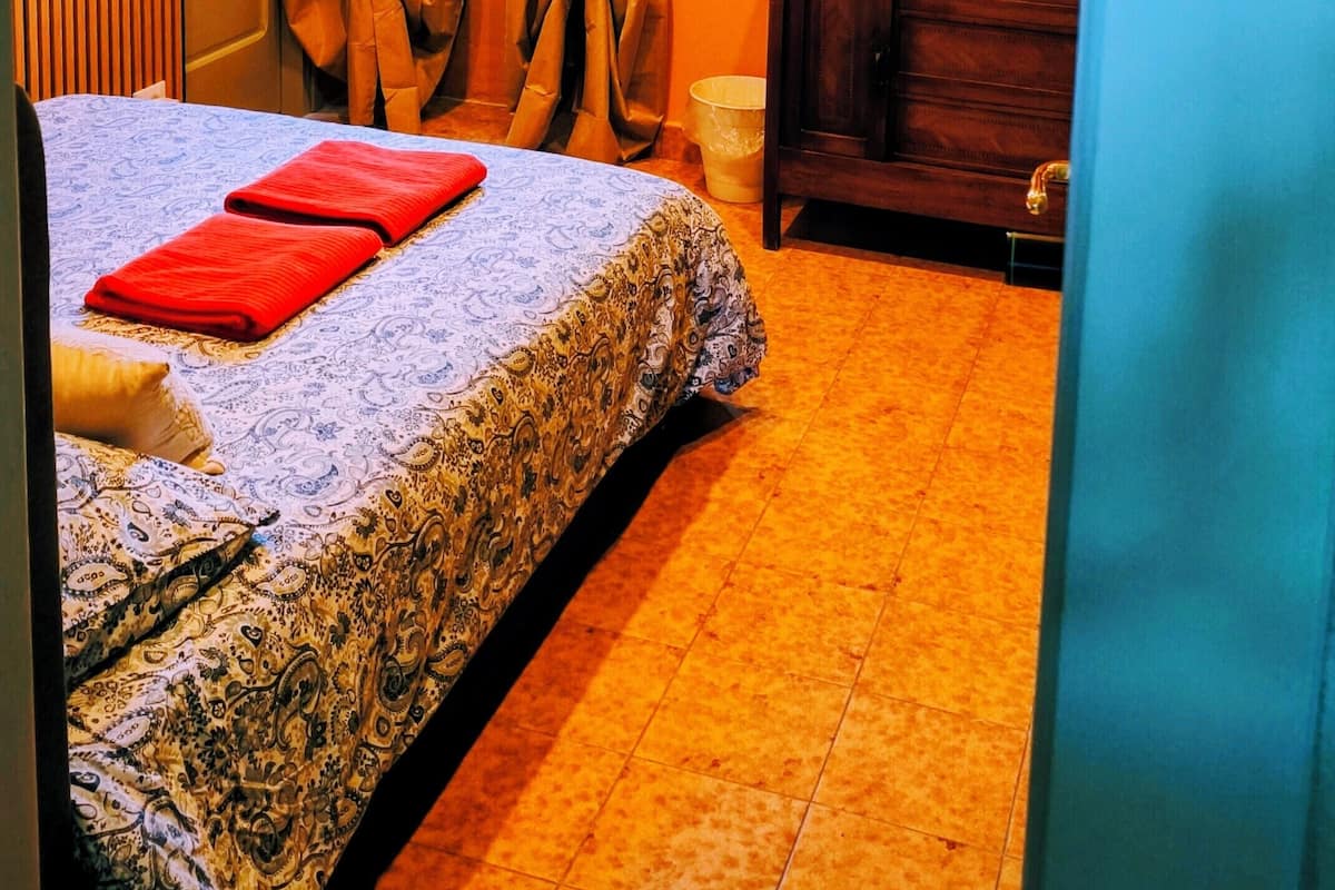 A bedroom with a bed, curtains, a dresser, a framed picture, and a door with a number.