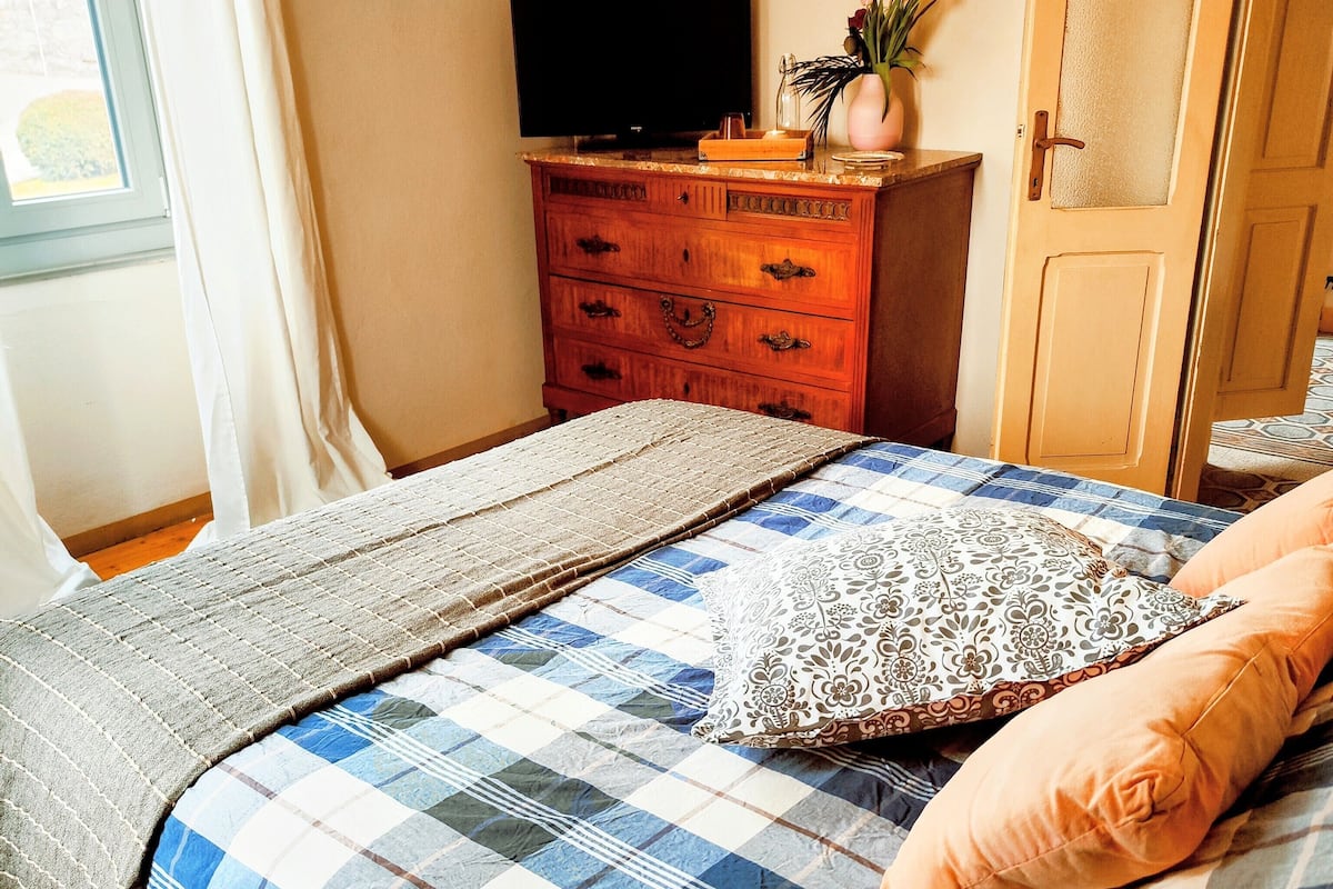 A bedroom with a bed, a dresser, a television, and a window with curtains.