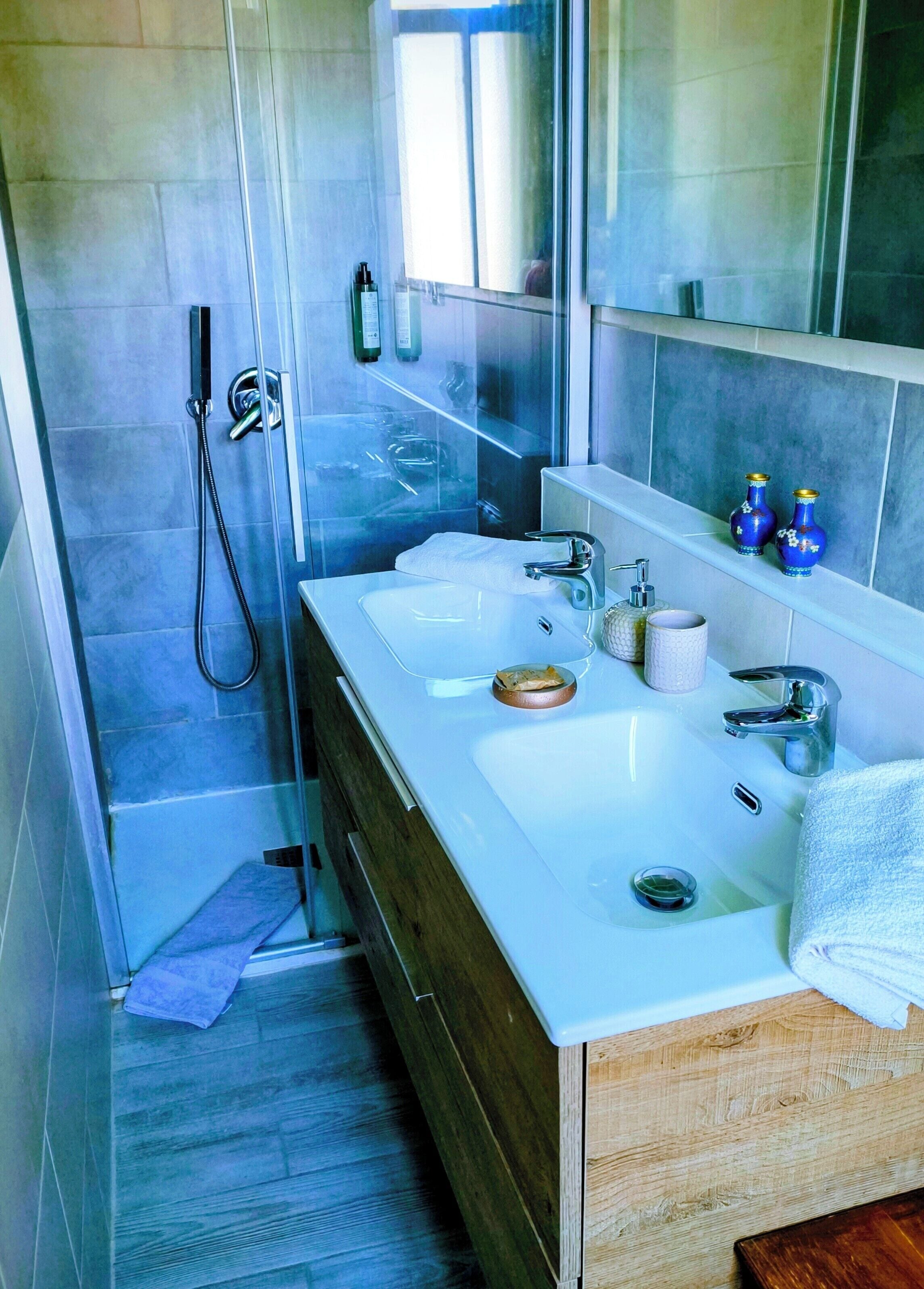 Een moderne badkamer met twee wastafels, een douche en een spiegel.