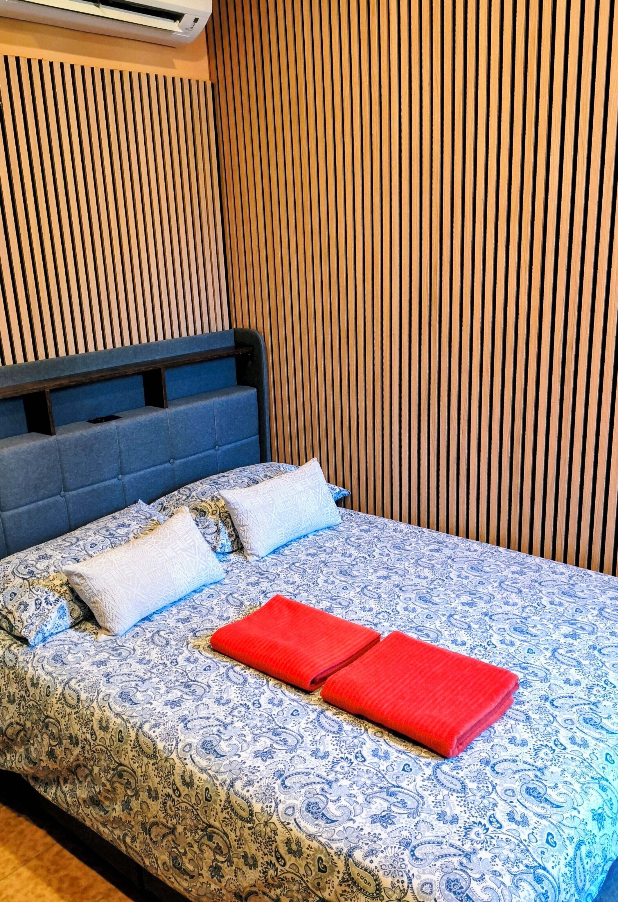 A bed with a patterned bedspread, pillows, and red towels.