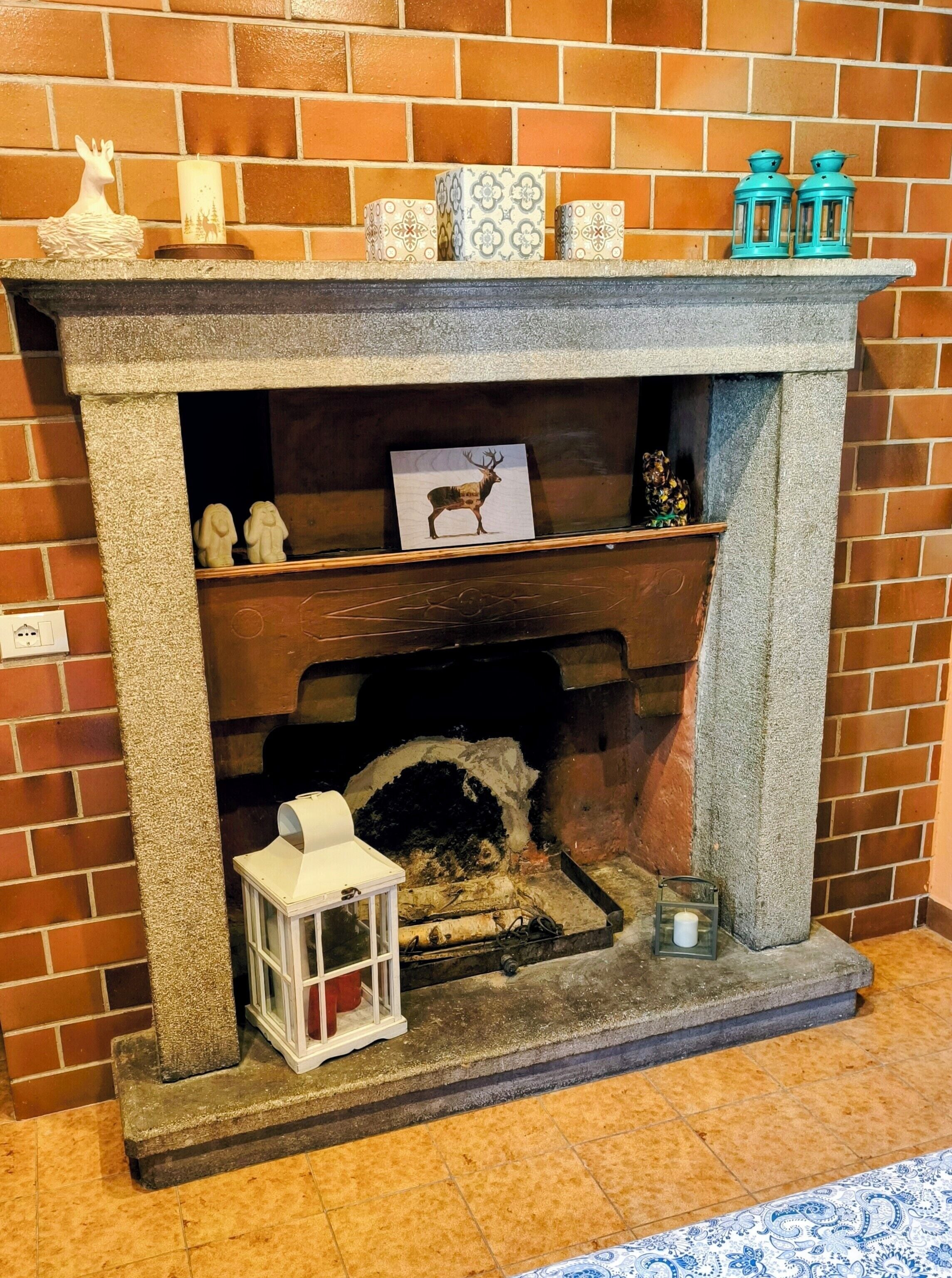 A fireplace with a brick wall backdrop, a shelf with decorative items, and a framed picture of an elk.