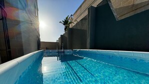 A clear blue swimming pool with a tiled floor, surrounded by walls and a palm tree. - Bayside (Marsaxlokk)