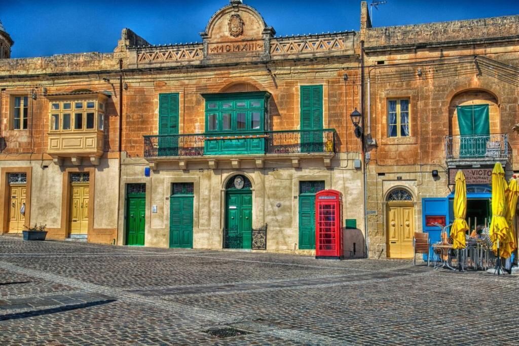 A historic building with green shutters, a red telephone booth, and outdoor seating.