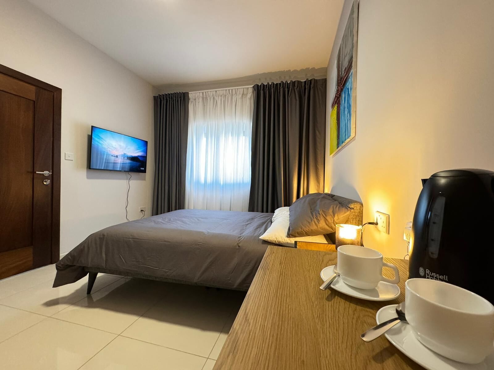 A hotel room with a bed, a television, a coffee maker, and a table with a cup and saucer.