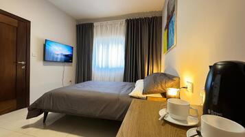 A hotel room with a bed, a television, a coffee maker, and a table with a cup and saucer.