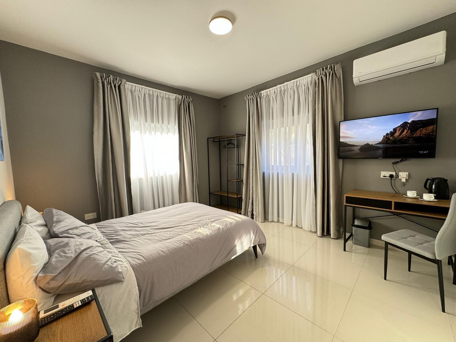 A hotel room with a bed, a desk with a chair, a television, and a shelf.