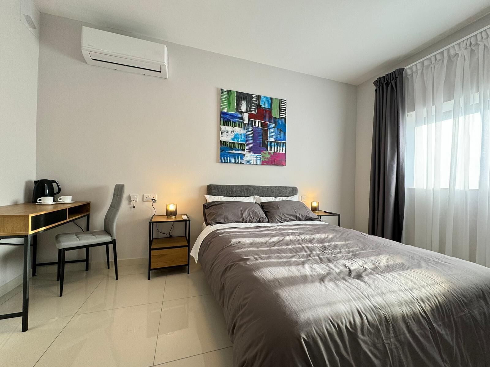 Une chambre d’hôtel moderne avec un grand lit, un bureau avec une chaise, une machine à café et un tableau au mur.